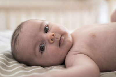 Close-up portrait of baby boy lying on bed at home