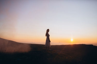 Side view of man standing on land against sky during sunset