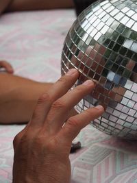 Cropped hands of person touching disco ball on bed 