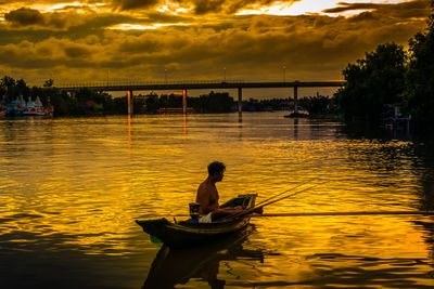 Silhouette man on boat in lake against sky during sunset