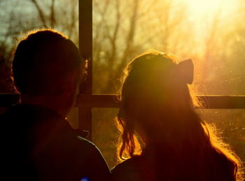 Rear view of couple looking through window during sunset