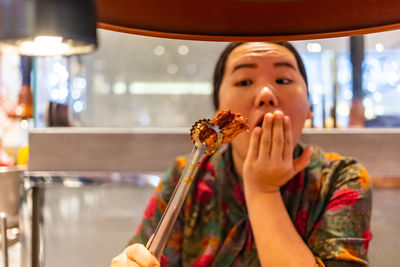 Shocked woman holding food by barbecue grill in restaurant