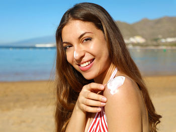 Portrait of smiling young woman applying sunscreen at beach