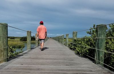 Rear view of man standing on railing against sky