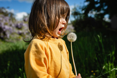 Girl in yellow clothes blowing a flower