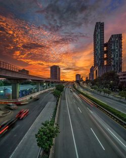 Road by buildings against sky during sunset