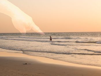 Man standing on beach against clear sky during sunset