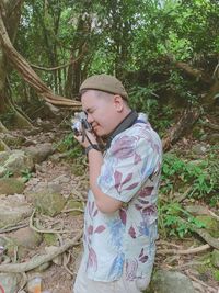 Man holding camera while standing by tree in forest