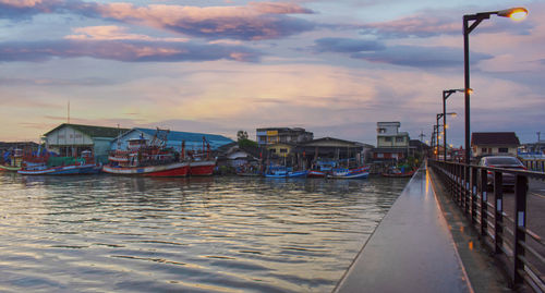 Boats moored on street by buildings against sky during sunset