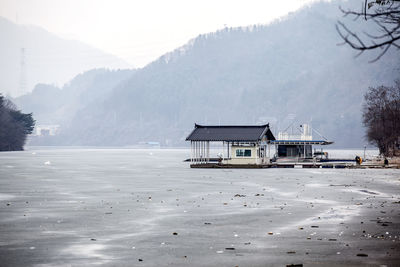 Cottage on frozen lake against mountains