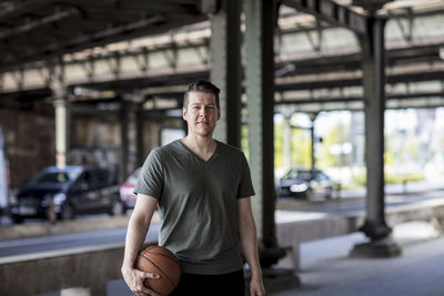 Portrait of young man with basketball standing on bridge