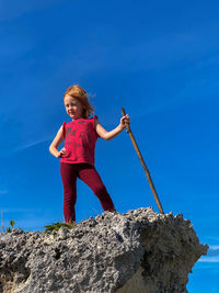 Low angle view of girl standing on rock against blue sky