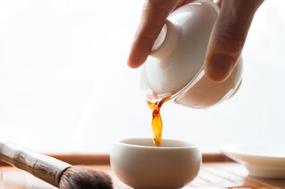 Cropped hand pouring tea in cup using teapot against white background