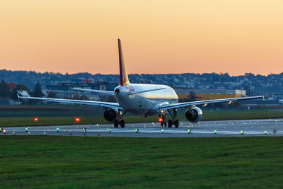 Airplane on airport runway against sky during sunset