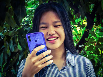 Portrait of smiling young woman using mobile phone outdoors