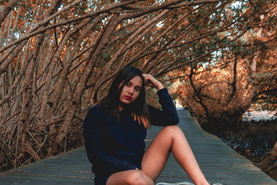 Portrait of young woman sitting on boardwalk amidst trees