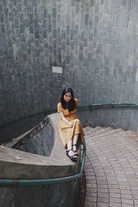 Portrait of woman sitting on railing wall by steps