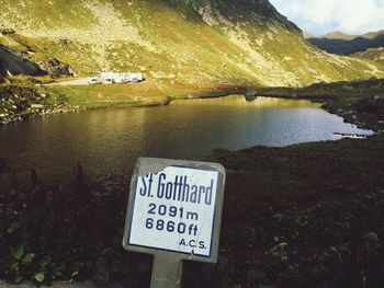 Close-up of information sign by lake against sky