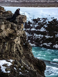 Man standing on rock by sea against sky during winter