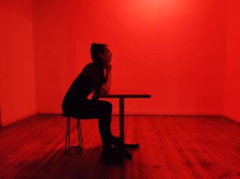 Side view of woman sitting on chair against wall