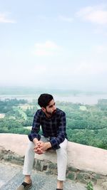 Full length of young man sitting on landscape against sky