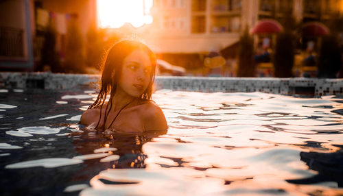 Thoughtful woman swimming in pool during sunset