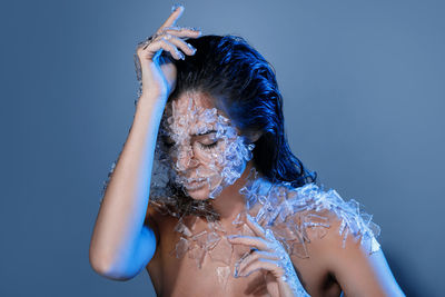 Close-up of woman with broken glass on body against purple background