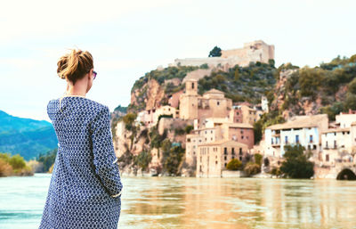 Rear view of woman standing by ebro river against miravet village