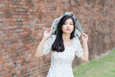 Portrait of a young woman standing against brick wall