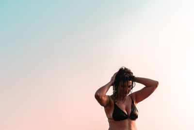 Wet woman with arms raised standing against clear sky during sunset