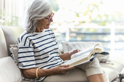 Woman reading book sitting on sofa at home