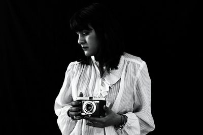 Thoughtful woman holding vintage camera against black background