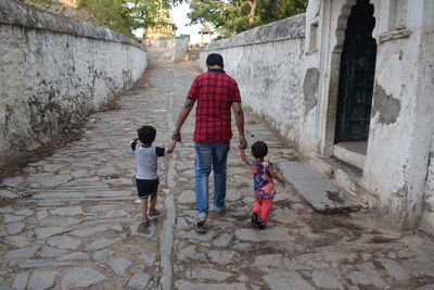 Rear view of father holding hands of kids while walking on street