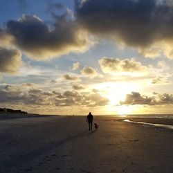 People walking on beach against sky during sunset