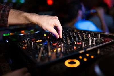 Cropped hand of dj using sound mixer at night