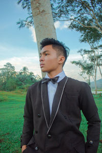 Young man looking away while standing on tree trunk