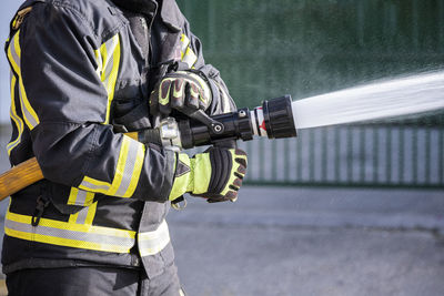 Midsection of firefighter holding fire hose outdoors