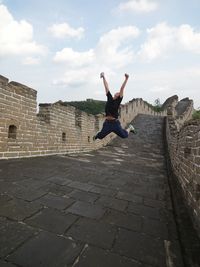 Full length of cheerful woman jumping on great wall of china against sky