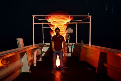 Man standing by illuminated lamp against black background