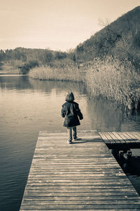 Full length rear view of girl walking on pier against river