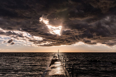 Pier in sea against cloudy sky at sunset