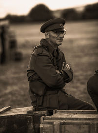 Soldier in uniform with arms crossed sitting by field on wood