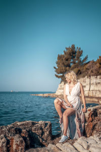 Woman sitting on rock by sea against clear sky