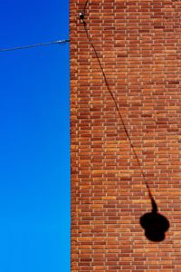 Low angle view of brick with a lamp shadow wall against clear sky