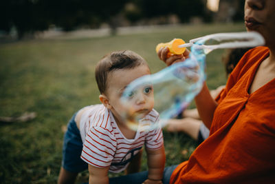Midsection of mother blowing bubble with son siting at park