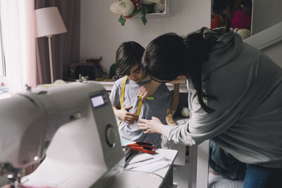 Mother sewing clothes for son at home