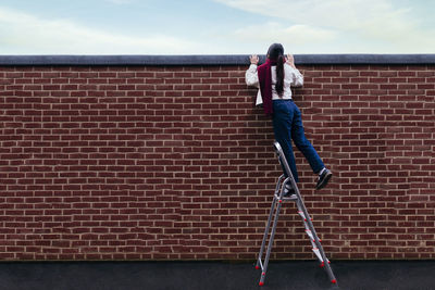 Young woman standing on ladder peeking over wall