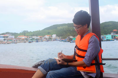 A young vietnamese man sitting on the boat writing notebook