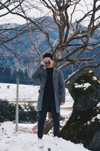 Man with camera standing on snow against trees