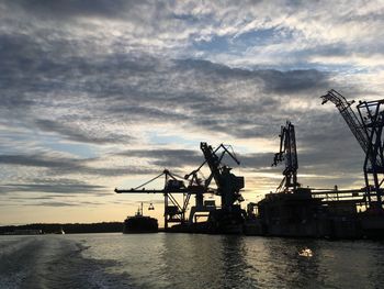 Silhouette cranes at commercial dock against sky during sunset